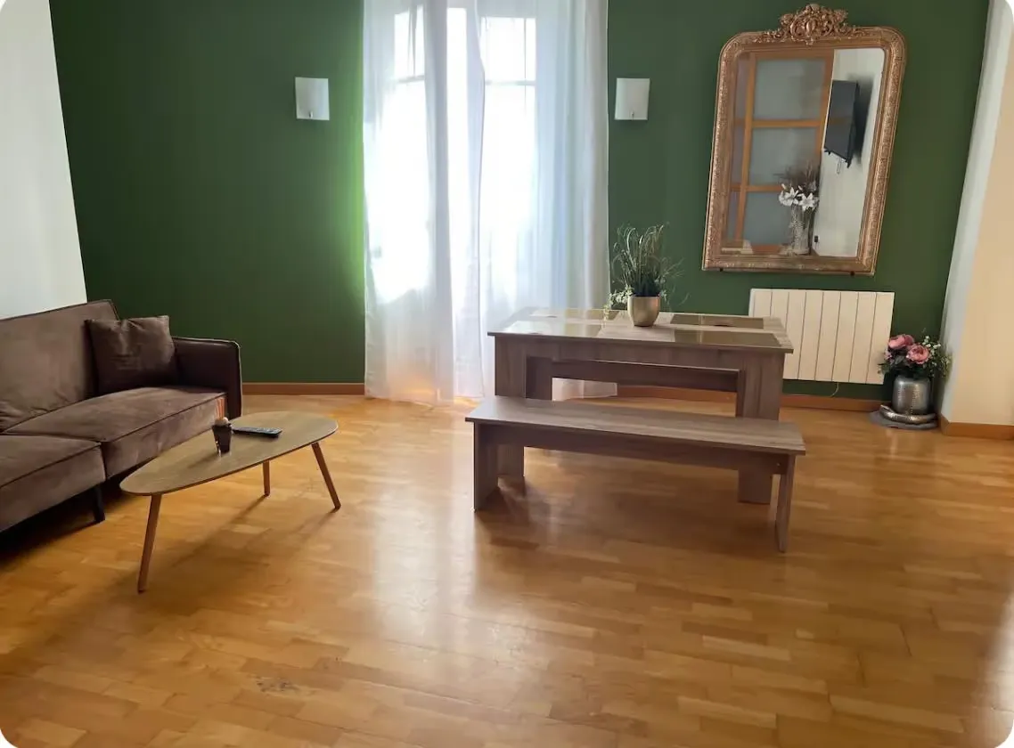 Séjour avec un mur peint vert profond, parquet et grand miroir doré